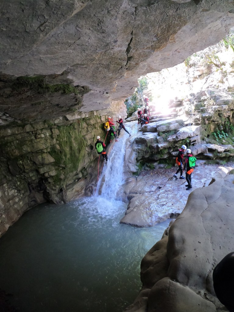 Une personne descend en rappel une cascade sous une grotte naturelle