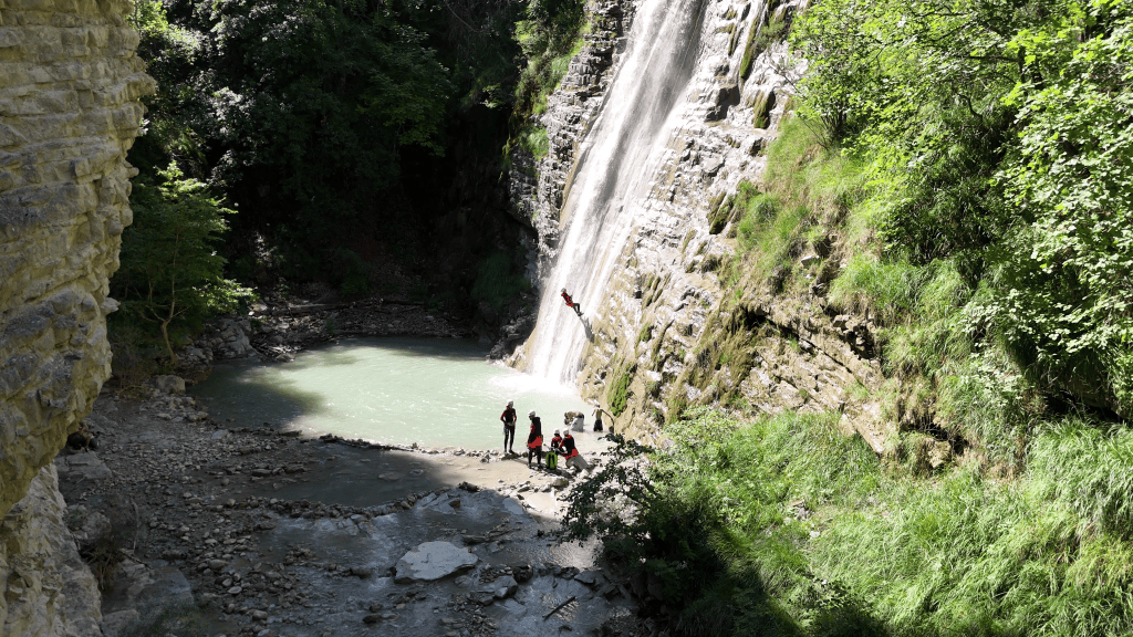 Une personne descend la belle cascade d'Entrevaux pendant que le reste du groupe se baigne dans une piscine naturelle au pied